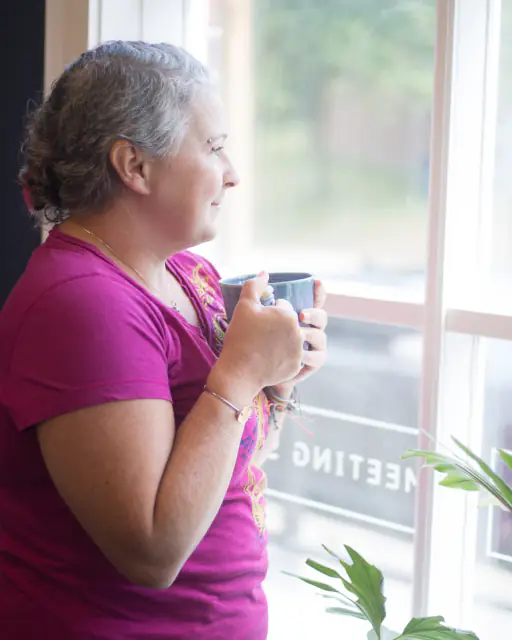 A woman holding a mug and looking out of a bright window