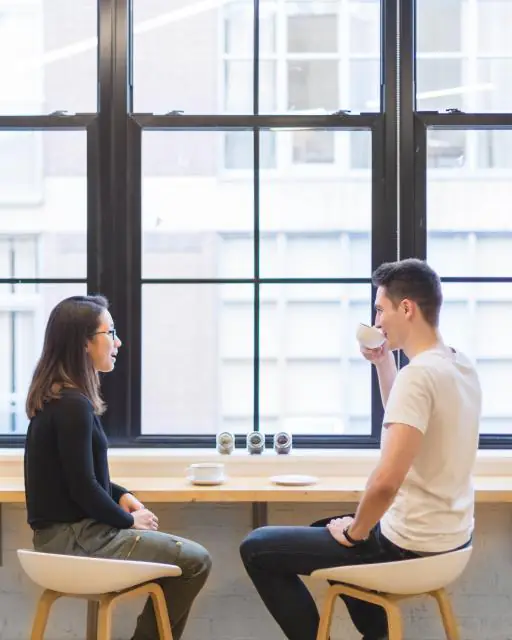 Two people chatting over drinks by a bright window