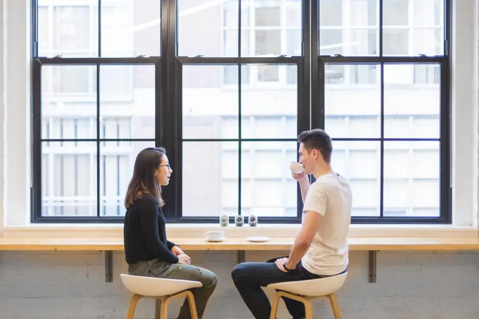 Two people talking calmly across a counter by a bright window